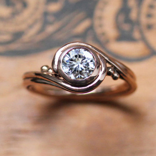 Rose gold ring with swirling features and faceted moissanite gemstone.