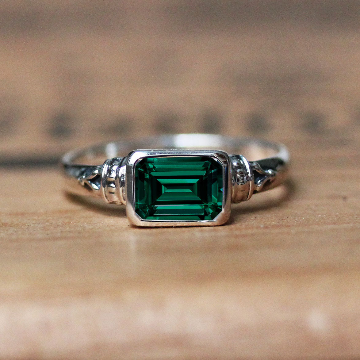 green emerald ring that is emerald cut and bezel set into a sterling silver vintage style setting